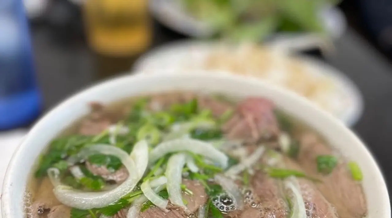 White bowl of Pho 45 beef pho topped with onions, scallions, and cilantro
