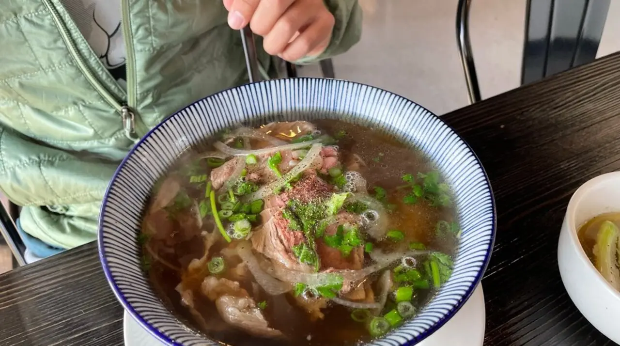 Blue-rimmed bowl of Pho REDBO wagyu beef pho with onions and black pepper in Garden Grove