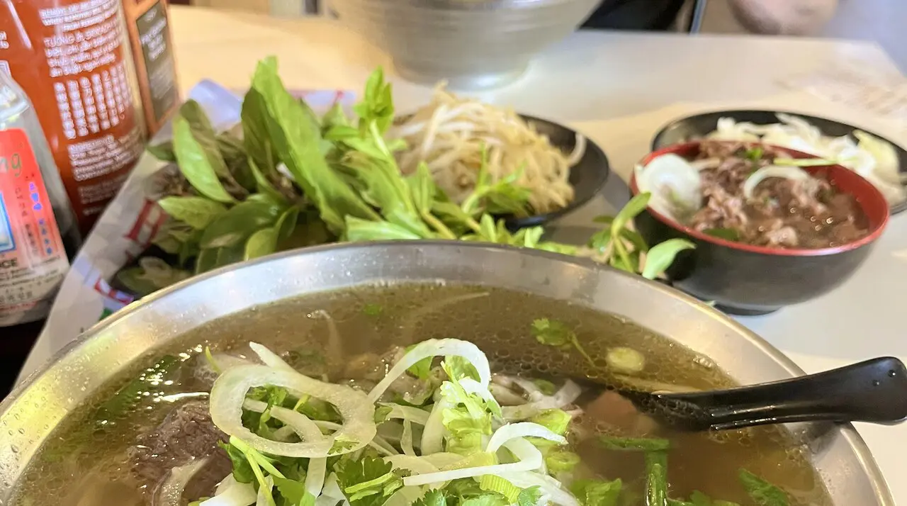 Metal bowl of Phoholic beef pho with onions, herbs, bean sprouts, and rare beef side